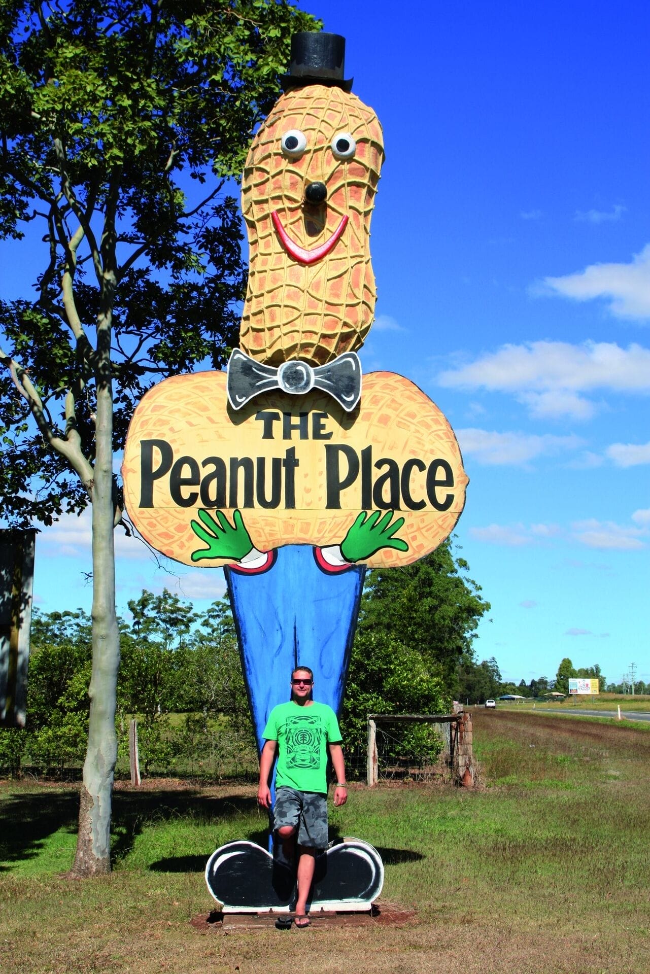 „Person steht vor einer großen, bunten Erdnussfigur mit der Aufschrift ‚The Peanut Place‘ am Straßenrand.“