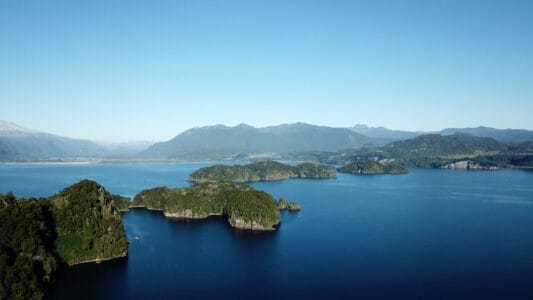 „Luftaufnahme vom See bei Puyehue in Chile mit grünen Inseln, Berglandschaft und blauem Himmel – Naturparadies für Erholung und Outdoor-Aktivitäten.“