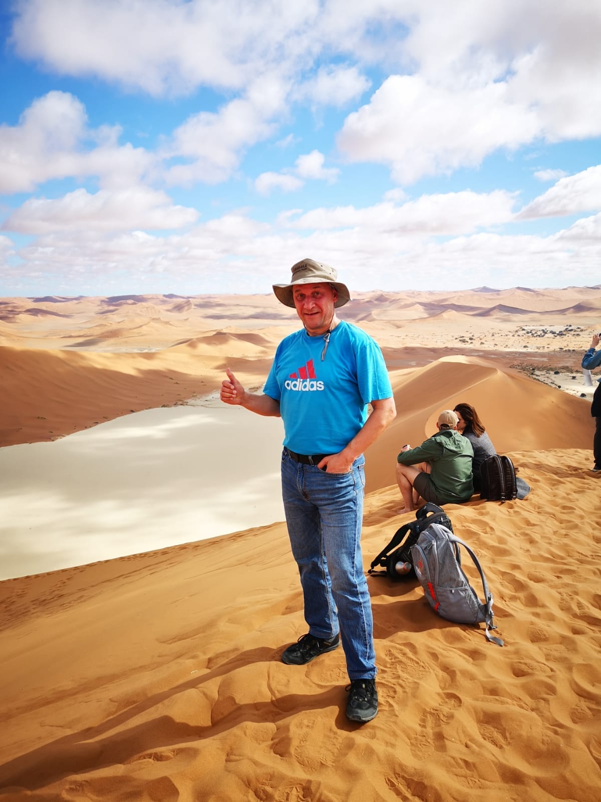 Sanddünen der Namib‑Wüste in Namibia mit Person auf einer hohen Düne und weitem Blick über die Wüstenlandschaft.