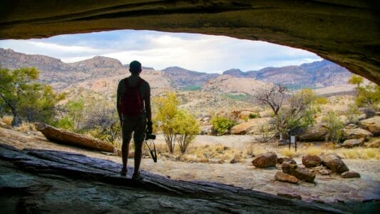 Wanderung im Erongo‑Gebirge in Namibia: Blick aus einer Felsüberdachung auf weite Granitlandschaft und Berge.