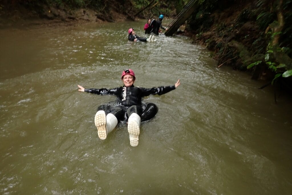 Black‑Water‑Rafting in Waitomo, Neuseeland: Person treibt im Gummireifen durch einen Fluss, ausgestattet mit Neoprenanzug, Helm und Gummistiefeln.