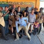 Gruppe von Menschen vor einem farbenfrohen Wandgemälde in Namibia, gemeinsames Gruppenfoto während einer Reise.