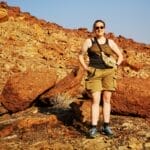 Wüstenlandschaft im Damaraland in Namibia mit Person auf felsigem Gelände unter blauem Himmel.