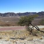 Aussicht am Spreetshoogte Pass in Namibia mit weiter Berg‑ und Wüstenlandschaft, Straße und windgeformtem Baum.